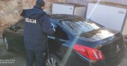 Na zdjęciu widoczny odzyskany pojazd marki Peugeot. Nad pojazdem stoi policjant ubrany w granatowy mundur wyjściowy i kurtkę z napisem Policja.