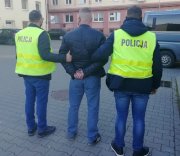 Nieumundurowani policjanci w żółtych kamizelkach z napisem POLICJA prowadzą zatrzymanego sprawcę rozboju,