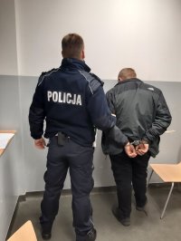 Policjant prowadzi zatrzymanego sprawce wypadku