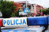 Radiowóz policyjny na tle przejścia dla pieszych i stojących tam policjantów.