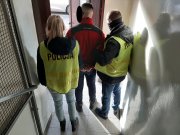 Dwóch policjantów z zielonych kamizelkach policyjnych z napisem Policja prowadzi zatrzymanego po schodach w kierunku wyjścia z policyjnego aresztu.