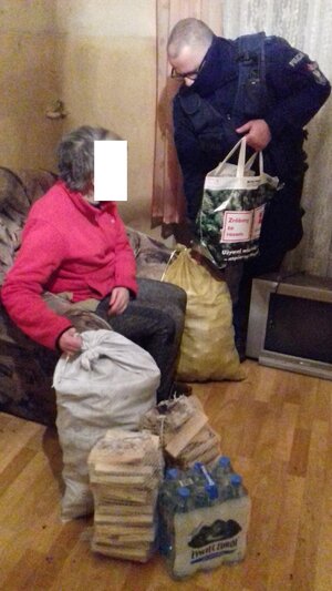 Policjant przekazuje seniorce artykuły żywnościowe i opał zebrany przez funkcjonariuszy.