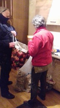 Seniorka wraz z umundurowanym policjantem, który przekazuje jej dary zebrane przez funkcjonariuszy - opał i jedzenie.