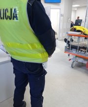 Policjant stoi na izbie przyjęć. W tle mężczyzna, któremu pomógł.