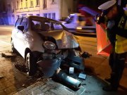 Policjant ruchu drogowego stojący przy rozbitym samochodzie- auto wbite w latarnię. Policjant robi zdjęcie. 
Zdjęcie wykonane w porze nocnej