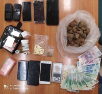 Na zdjęciu widzimy leżące na biurku narkotyki w kształcie brązowych kulek, pieniądze, telefony komórkowe, żółte tabletki oraz w przeźroczystej torebce fiolki z anabolikami.