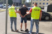 Mężczyzna jest odwrócony tyłem, ma spuszczoną głowę , jest trzymany po obu stronach przez policjantów i prowadzony do nieoznakowanego radiowozu.