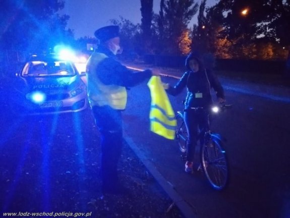 Policjant przekazuje rowerzyście kamizelkę odblaskową