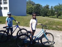 Chłopiec z dziewczynką w kaskach rowerowych stoją przy swoich rowerach. Dziewczynka ma białą koszulkę, chłopiec niebieską , mają po około 10 lat.