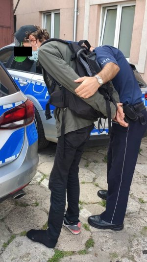 Policjant przeszukuje odzież jednego z mężczyzn posiadającego dopalacze.