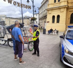 Ulica Piotrkowska, policjantka ruchu drogowego przy radiowozie kontroluje osoby.