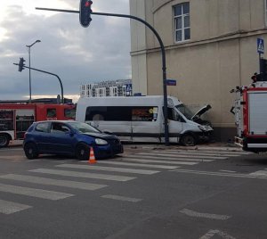 Miejsce wypadku, na jedni stoją rozbite pojazdy oraz wozy strażackie.