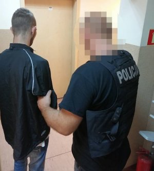 Policjant prowadzi podejrzanego korytarzem komisariatu.