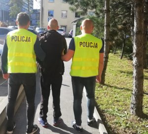 Policjanci prowadzą mężczyznę podejrzanego o kradzież aut.