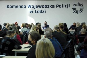 napis na ścianie Komenda Wojewódzka Policji w Łodzi, za stołem prezydialnym siedzi dwóch mundurowych, jeden generał zabiera głos mówiąc przez mikrofon, sala wypełniona jest pracownikami cywilnymi