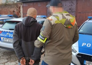 Policjant prowadzi do radiowozu zatrzymanego sprawce rozboju.