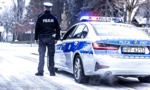 umundurowany policjant stoi przy oznakowanym radiowozie