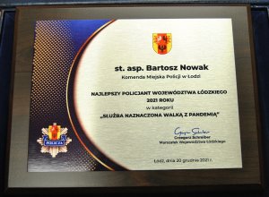 Tabliczka z napisem &quot;służba naznaczona walką z pandemią&quot; dla najlepszego policjanta województwa łódzkiego 2021 roku