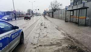 Radiowóz stojący przy zabłoconej jezdni i chodniku.