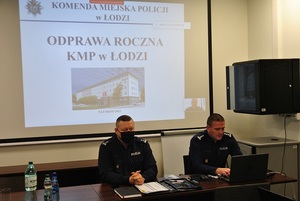 Komendant Miejski Policji w Łodzi wraz z jednym zastępcą w tle rzutnik z napisem odprawa roczna KMP w Łodzi.