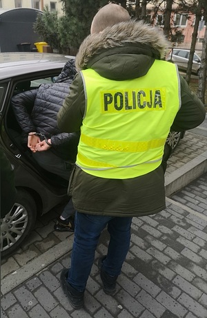 Zatrzymany wsiada do nieoznakowanego radiowozu w asyście policjanta.