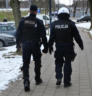 Zabezpieczenie meczu, policjanci , jeden w kasku ochronnym idą po chodniku.