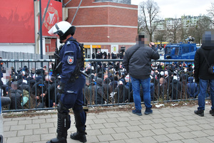 Eskorta kibiców gości, wokół policjanci zabezpieczający imprezę i radiowozy specjalistyczne.