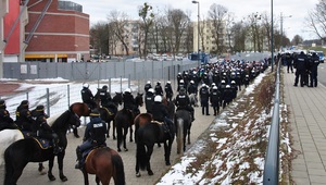 Służby podczas zabezpieczenia w tym sekcje konne. Przed nimi zgromadzeni przed wejściem kibice.