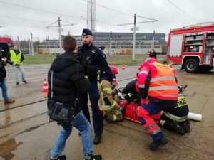 Uczestnicy podczas symulacji katastrofy, policjant odgradza gapiów , medycy udzielają pomocy pokrzywdzonym.