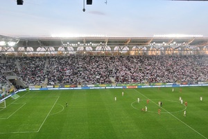 Spotkanie sportowe na murawie piłkarze Widzewa Łódź i ŁKS Łódź w tle trybuny z kibicami.