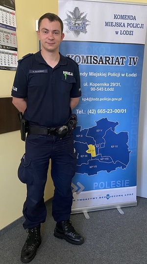 Dzielnicowy w umundurowaniu służbowym stoi na tle rolapu z danymi IV Komisariatu Policji w Łodzi.