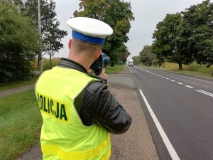 policjant ruchu drogowego stoi przy drodze z urządzeniem do pomiaru prędkości