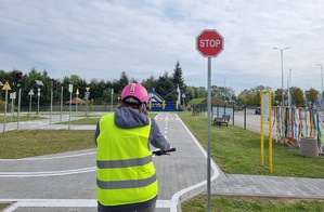 Rowerzysta  kasku stoi przed znakiem STOP na terenie miasteczka ruchu drogowego.
