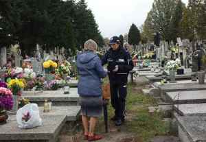 policjantka w mundurze daje ulotkę pani sprzątającej na cmentarzu grób
