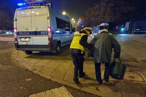 Policjantka prowadzi seniora do radiowozu.