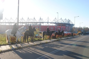 Policjanci i funkcjonariusze Straży Miejskiej na koniach zabezpieczają imprezę, stoją wokół stadionu.