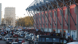 Zabezpieczenie meczu, wejście na stadion, zaparkowane samochody i kibice zgromadzeni przed wejściem.