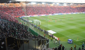 Stadion Widzewa, na murawie piłkarze, po lewej stronie sektor z kibicami gości.