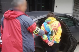 Policjant wprowadza do radiowozu podejrzaną.