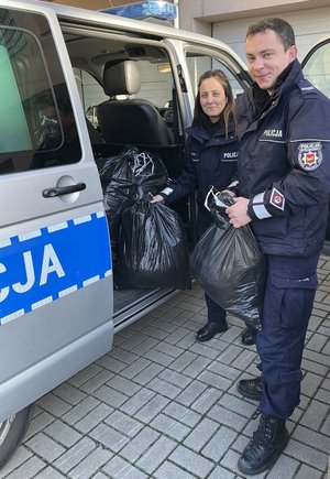 Policjanci pakują do radiowozu zebraną odzież.