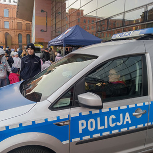 Radiowóz policyjny, w którym siedzi uczestniczka pikniku, za radiowozem stoi policjantka.