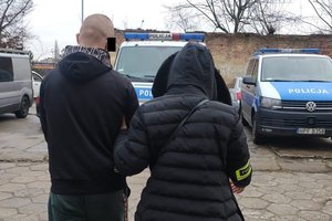 Nieumundurowana policjantka prowadzi sprawcę do radiowozu.