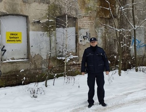 Policjant stoi przed pustostanem.