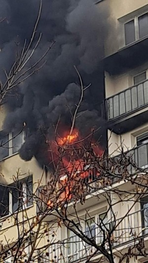 Okno mieszkania objętego pożarem, dym i ogień wydobywający się z okien w wieżowcu.