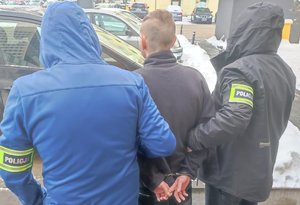 Dwaj nieumundurowani policjanci prowadzą zatrzymanego mężczyznę.