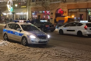 radiowóz policyjny jedzie ulicą, w tle taksówki stojące na postoju