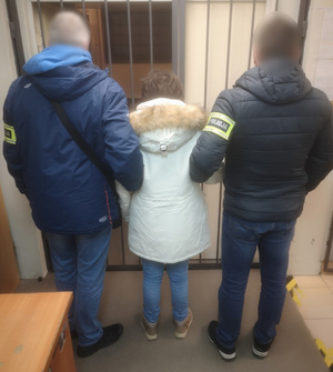 Policjanci prowadzą zatrzymaną kobietę.
