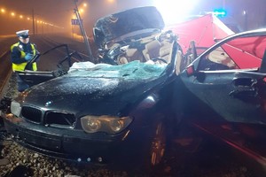 Miejsce wypadku, wrak samochodu leżący na torowisku tramwajowym, ratownicy pracują na miejscu wypadku.