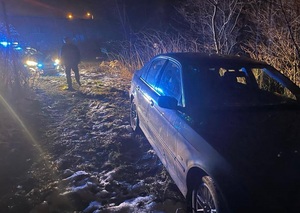samochód stoi na trawniku, z tyłu postać policjanta, w oddali radiowóz na sygnałach