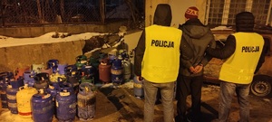 Policjanci w kamizelkach z napisem policja przy butlach z gazem.
